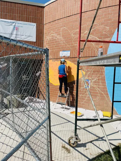 Anna Hileman on a ladder filling in the Wingate Elementary mural beside the D51 academic growth banner