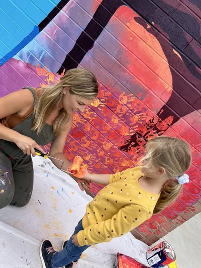 Artist rolling paint onto a student’s hand for a handprint on the Wingate Elementary mural wall