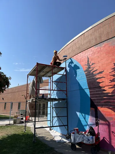 Anna Hileman on scaffolding painting the Wingate Elementary exterior mural
