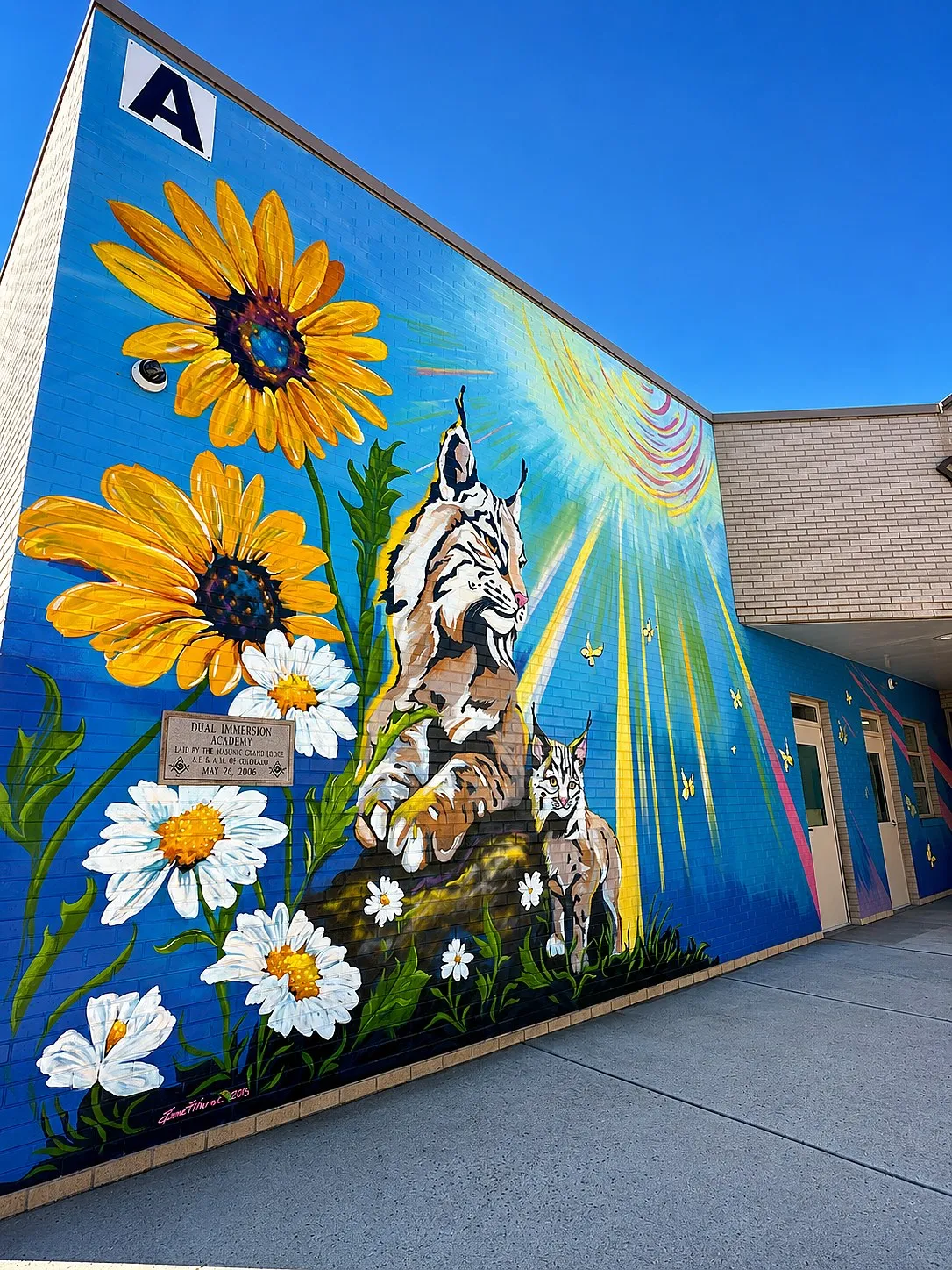 Dual Immersion Academy exterior brick mural featuring sunflowers, daisies, bobcats, and butterflies